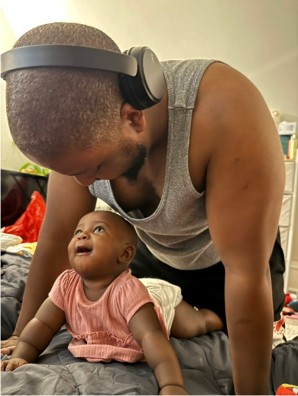 A father with headphones leaning down toward his baby daughter who looks up at him with pure delight — a Dad-Beats moment of presence and joy