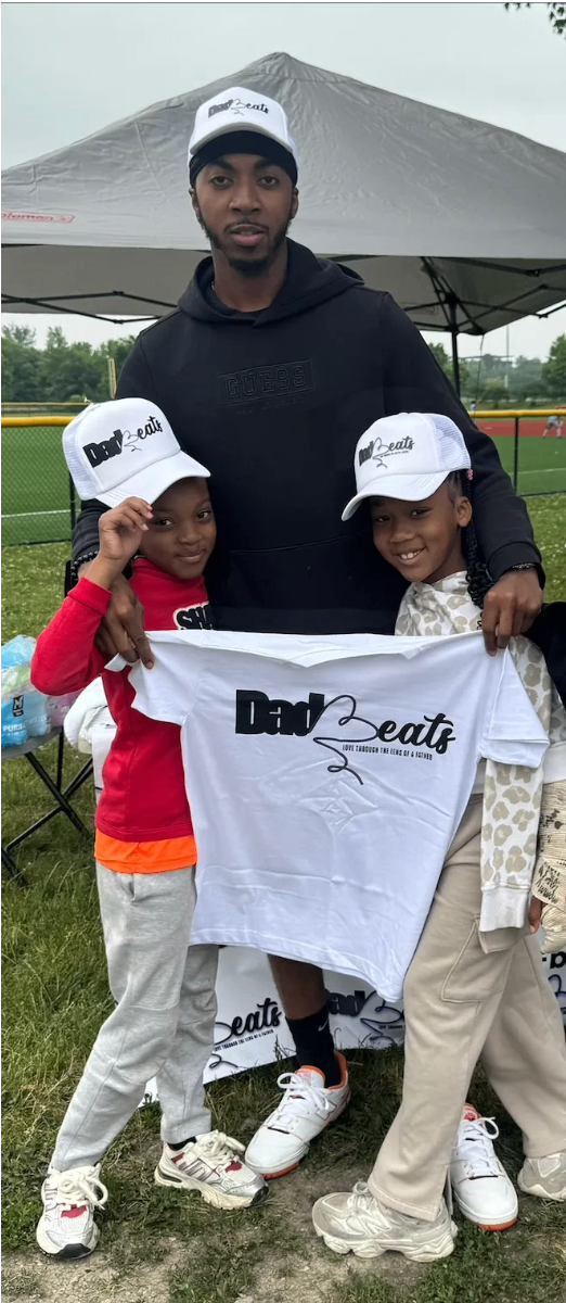 Father in a Dad-Beats hoodie with two daughters holding up a Dad-Beats shirt at the competition tent