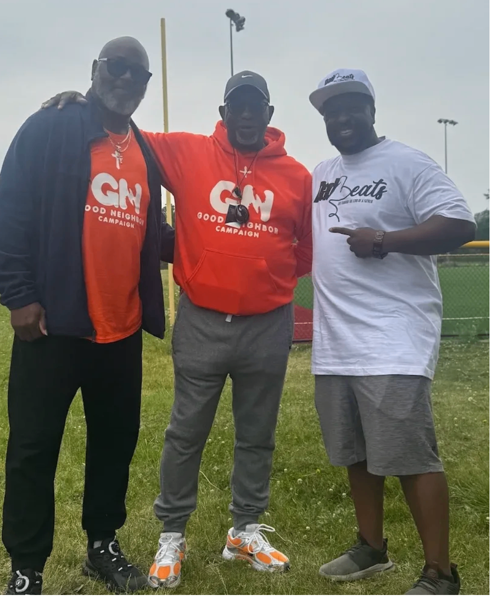 Two men in Good Neighbor Campaign shirts and a man in a Dad-Beats shirt standing together at the competition field
