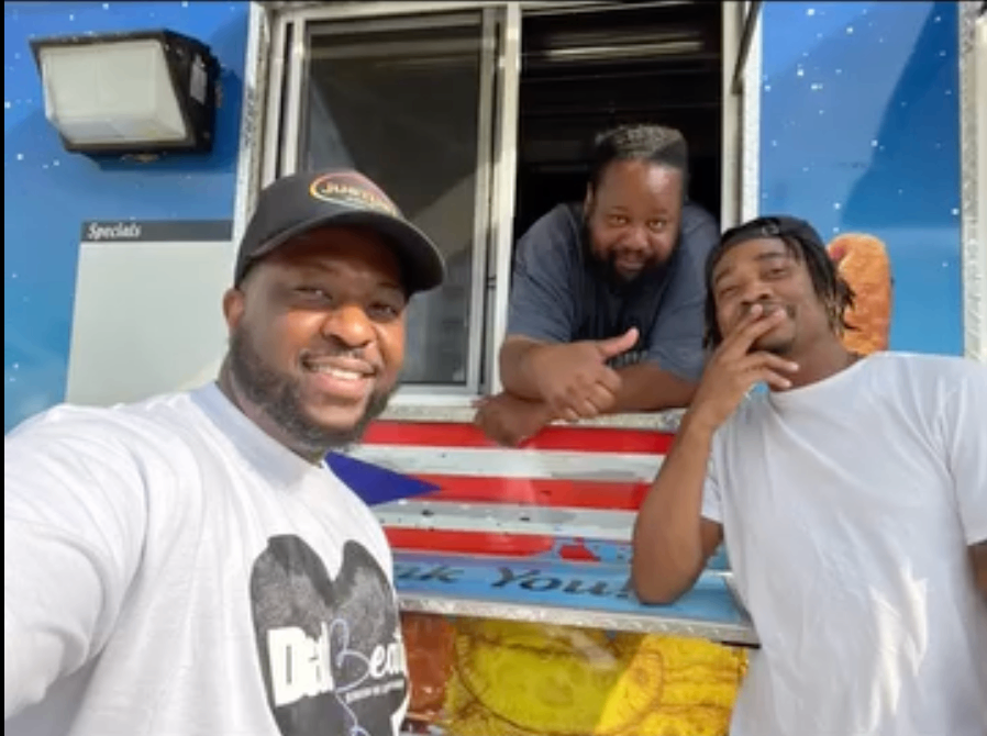 Three men hanging out together at a food truck, one wearing a Dad-Beats shirt
