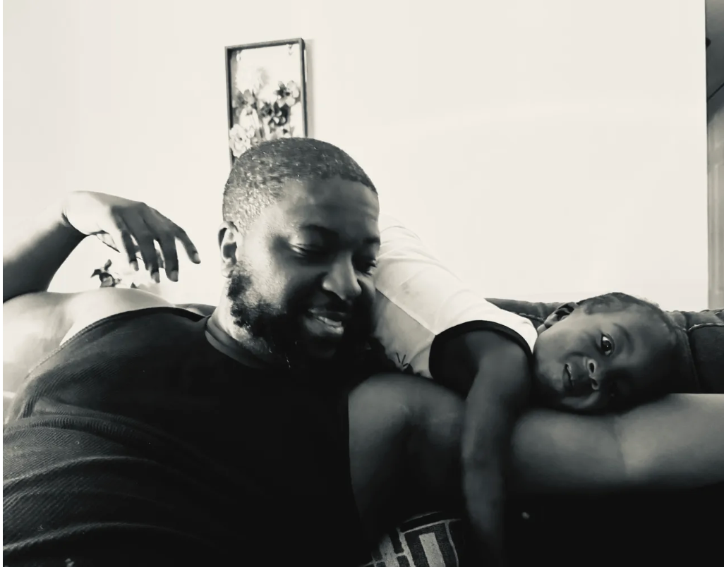 Dr. Marcus Rushing laughing as his young son rests across his shoulders — a quiet moment of joy and closeness